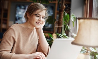 Cheerful young caucasian girl in glasses using laptop, shopping online 